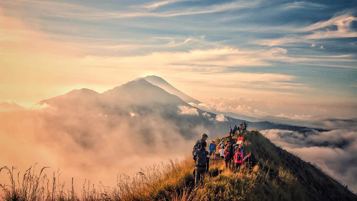 Hikers watching first light from the crater rim on a Mount Batur sunrise hike tour above Lake Batur, Kintamani, Bali